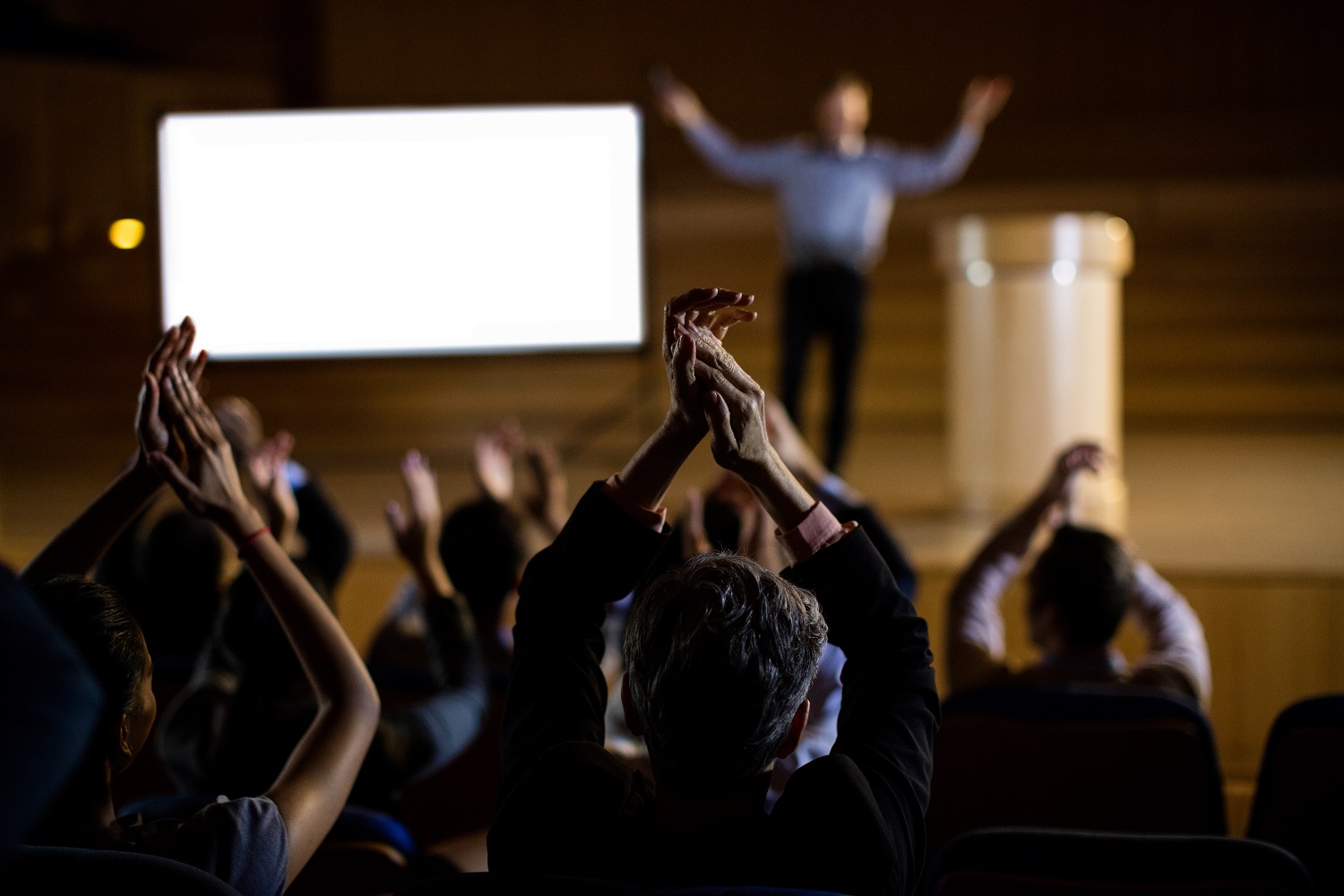 Pessoa aplaudindo o orador em palestra internacional com tradução simultânea.