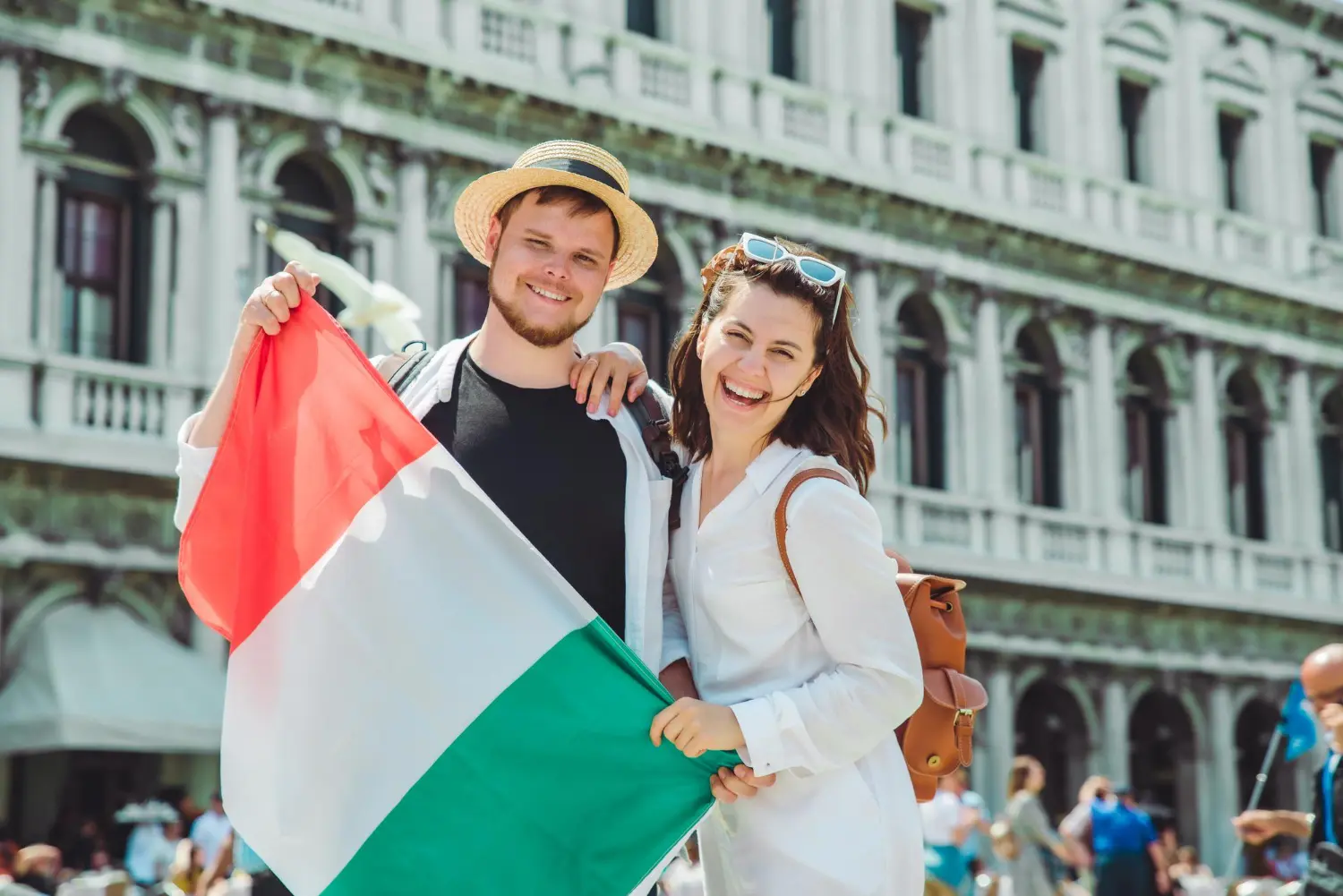 Jovem casal com bandeira italiana, felizes, após descobrirem como morar na Itália.