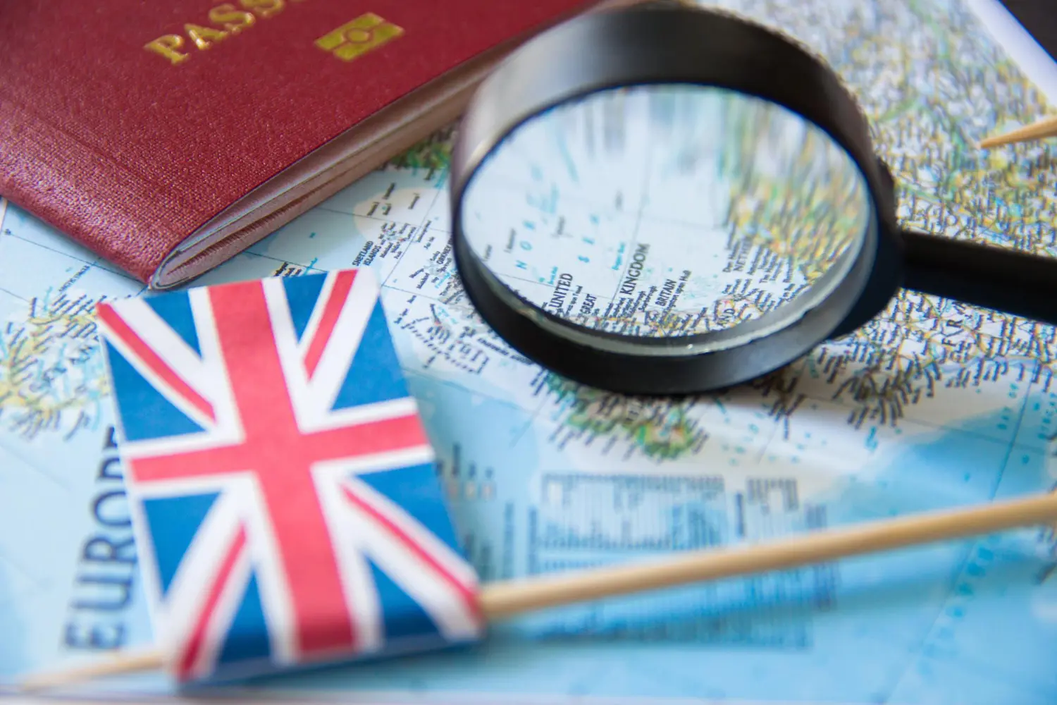 Passaporte e bandeira do Reino Unido sobre mapa com lupa, indicando local para morar no Reino Unido.