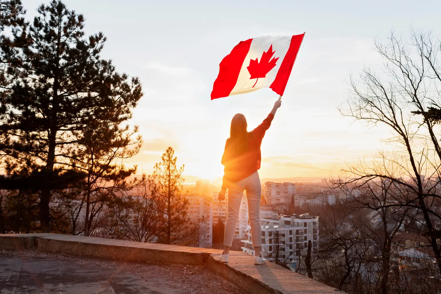 mulher com a bandeira do Canadá levantada, contemplando o pôr-do-sol
