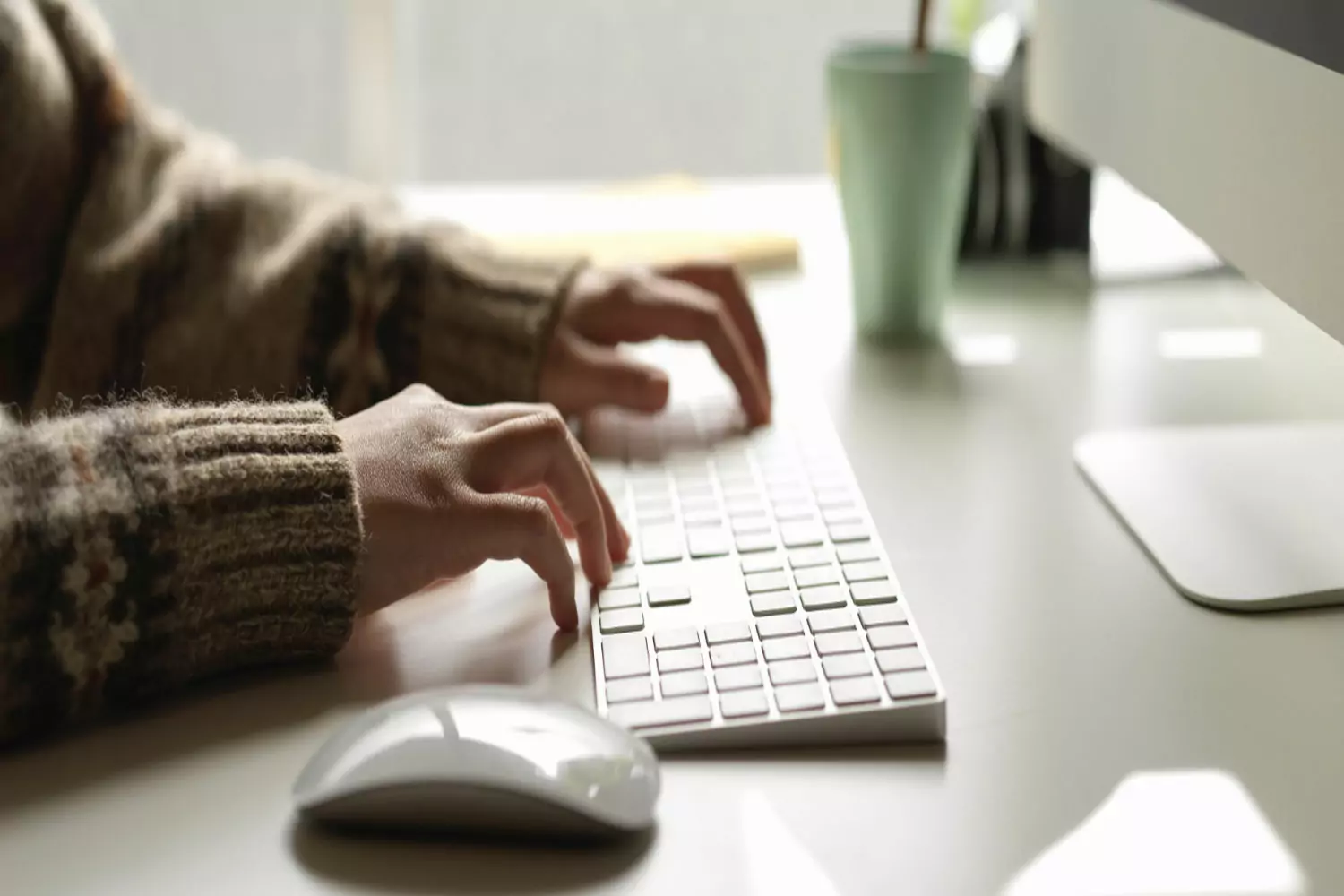Mãos de uma pessoa digitando em um teclado de computador sobre uma mesa.