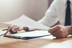 Tradutor italiano segurando um documento com outros documentos em sua frente, sobre a mesa.