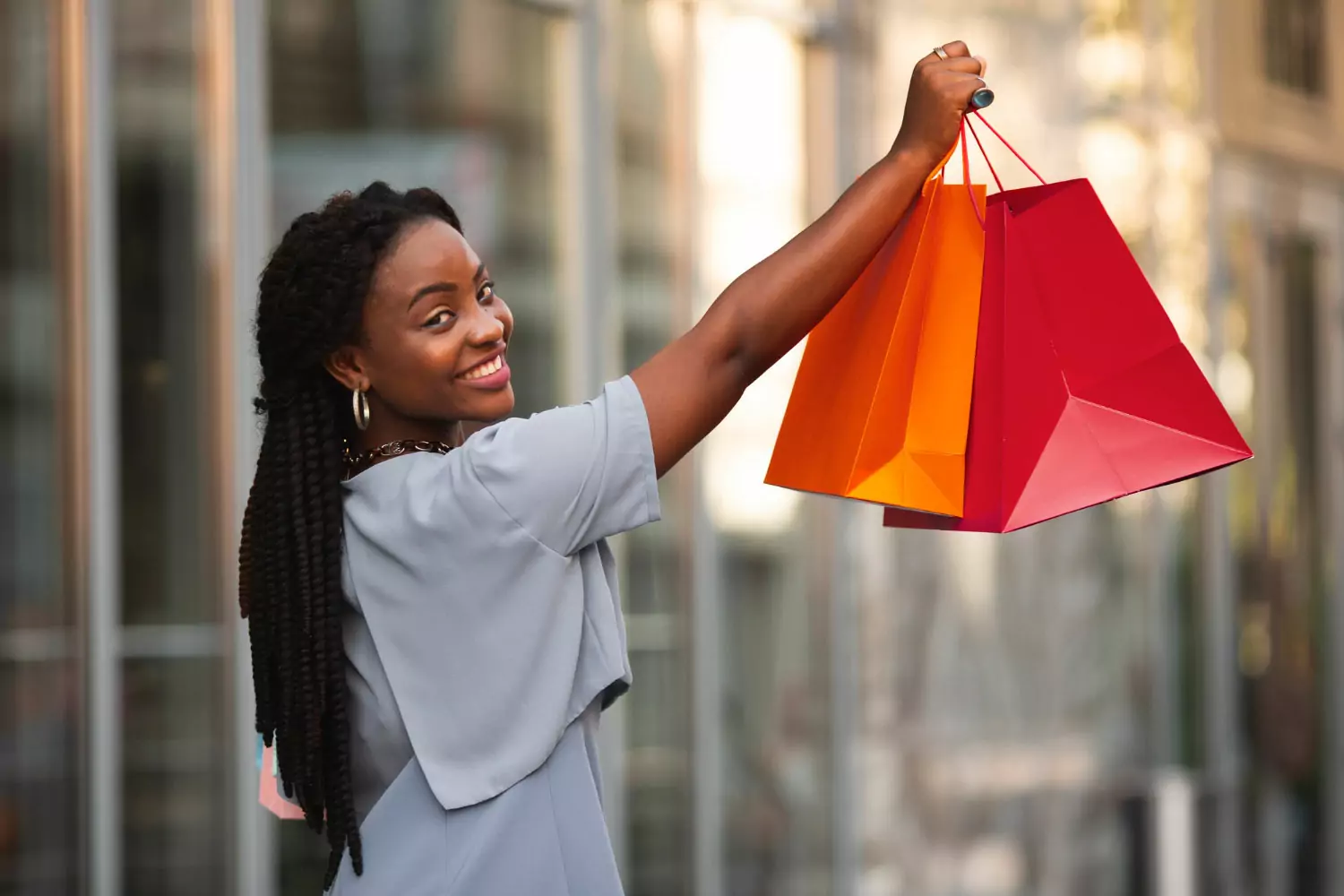 Mulher sorrindo, segurando sacolas no alto, respeitando o limite de compras no exterior.